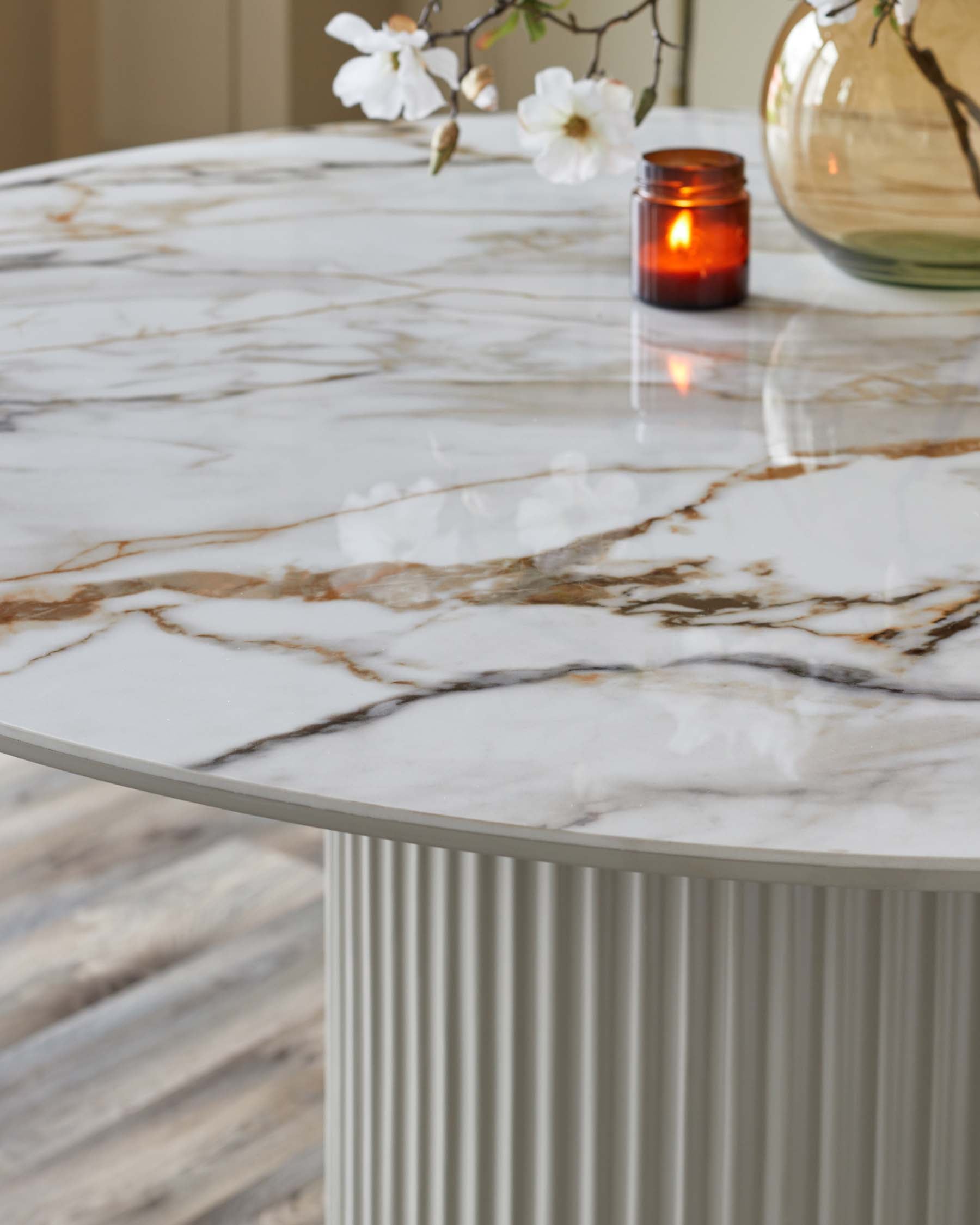 Elegant round marble table with a ribbed base, accented by a vase and a candle, enhancing its modern sophistication.