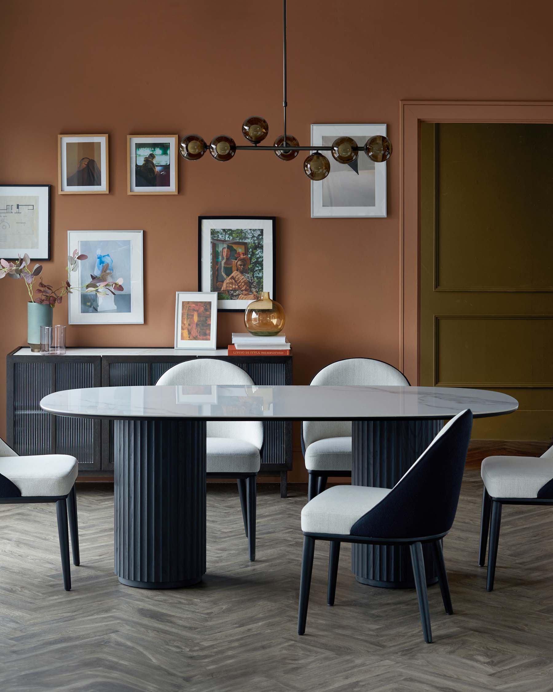 Sleek oval dining table with ribbed base, surrounded by stylish upholstered chairs; modern decor with wall art.