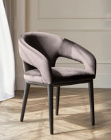 Sleek gray upholstered chair with curved arms and slender black legs, set against a light, airy backdrop.