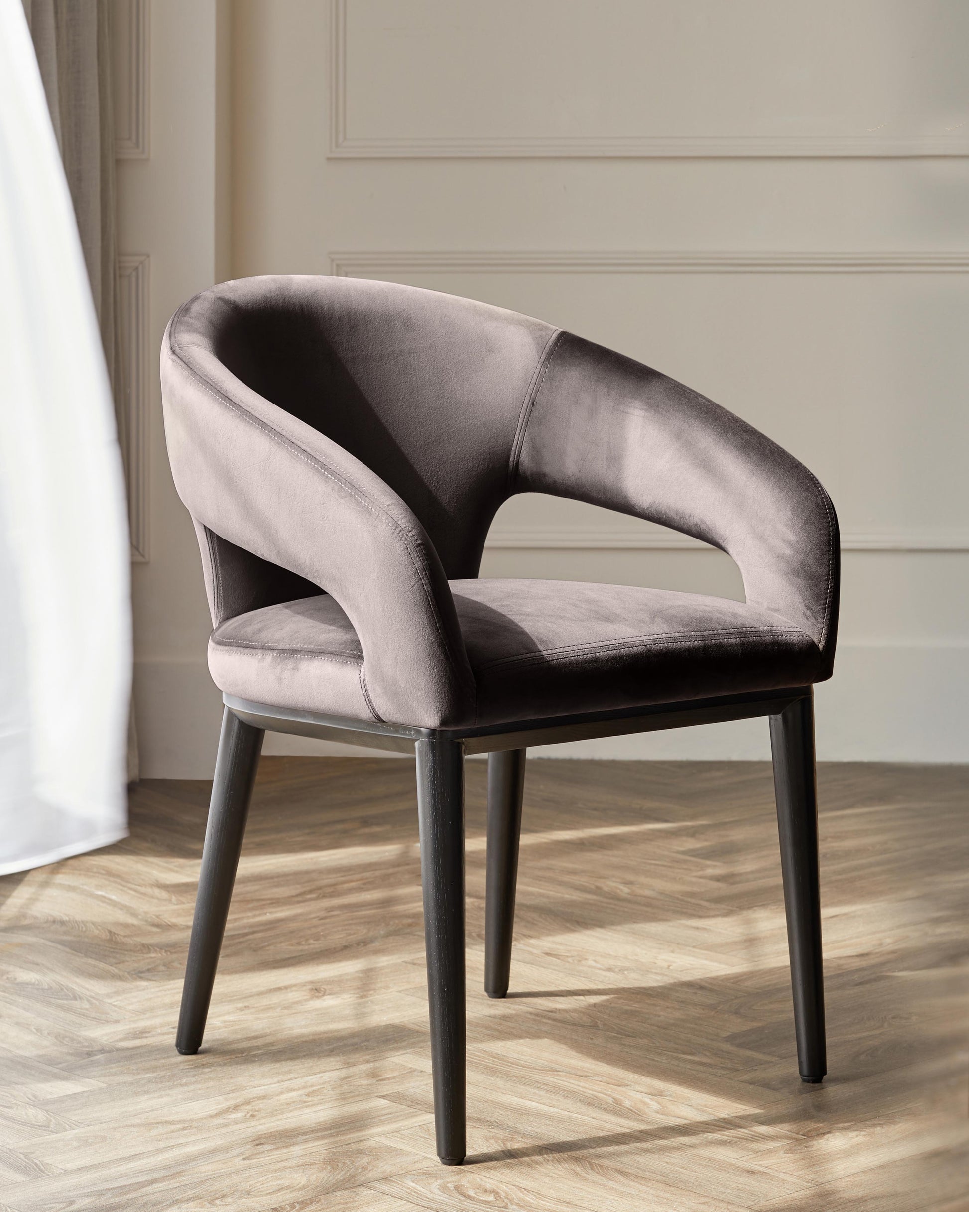 Sleek gray upholstered chair with curved arms and slender black legs, set against a light, airy backdrop.