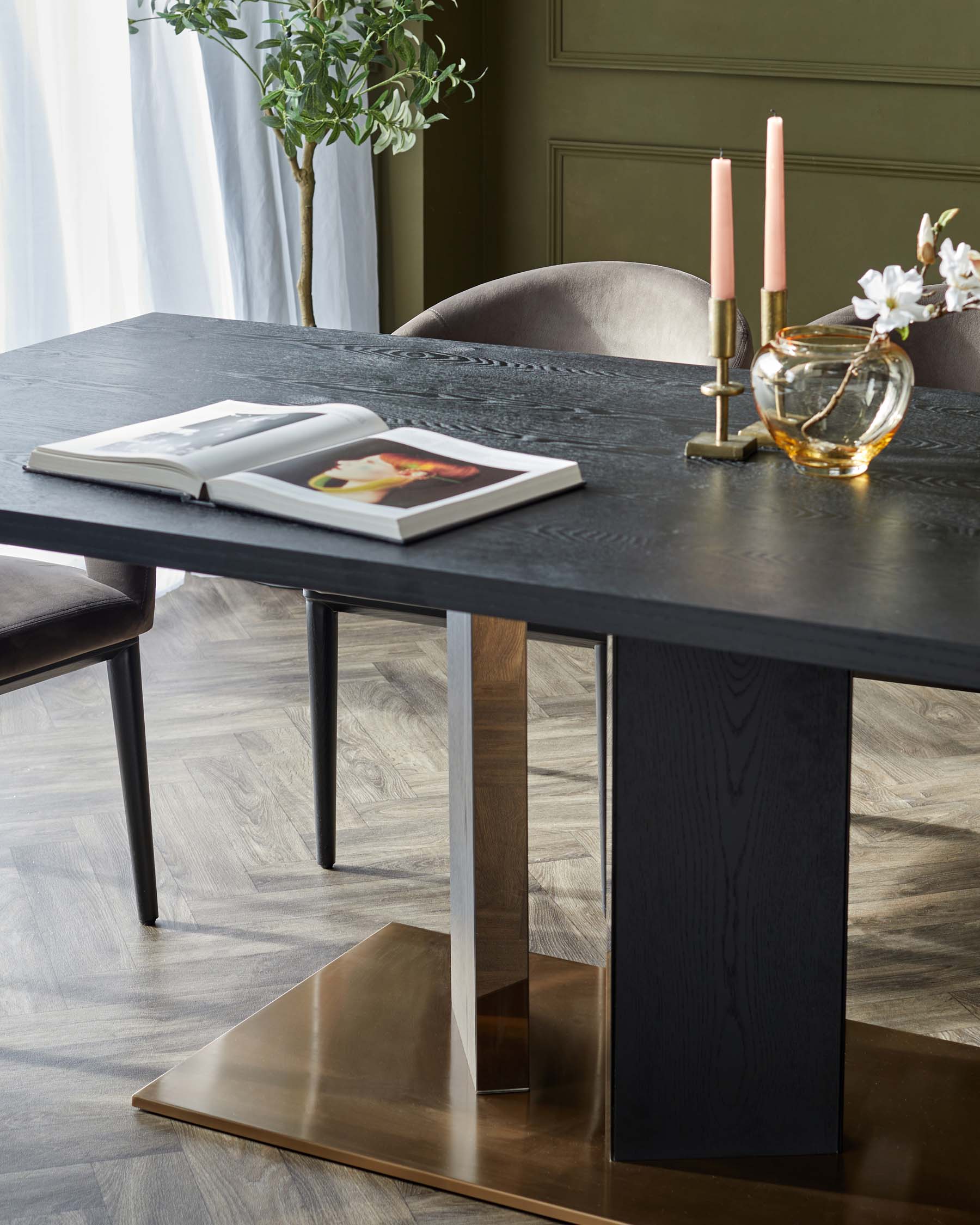 Elegant black dining table with a sleek brass base, surrounded by plush velvet chairs, accented by candles and floral décor.